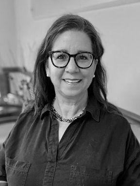 Smiling woman with glasses wearing a dark button-up shirt in a black-and-white photo.