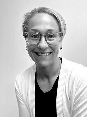 Smiling woman with short light hair and glasses, wearing a white cardigan over a black top.