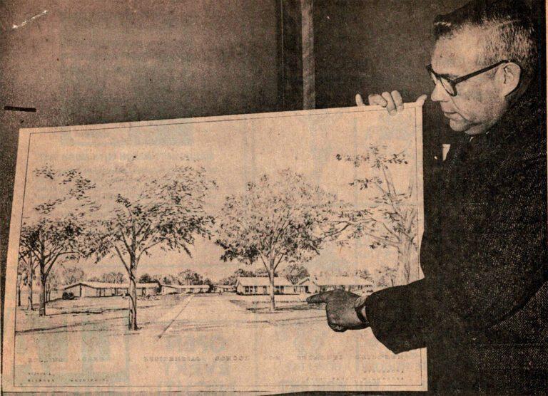 A man wearing glasses holds up a large drawing of a park landscape with trees.