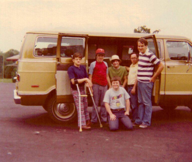 A group of children posing in front of a vintage tan van with its sliding side door open.