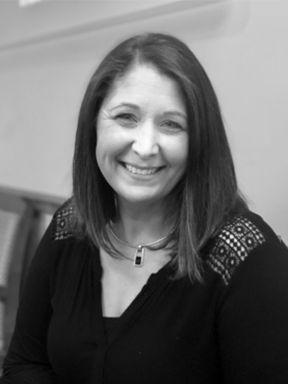 Smiling woman with shoulder-length hair wearing a black top and pendant necklace.
