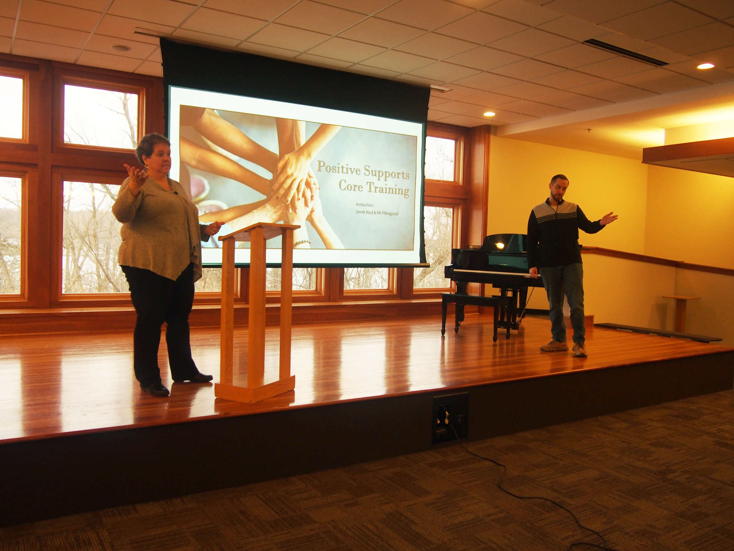 Two people on stage gesturing to screen with presentation.