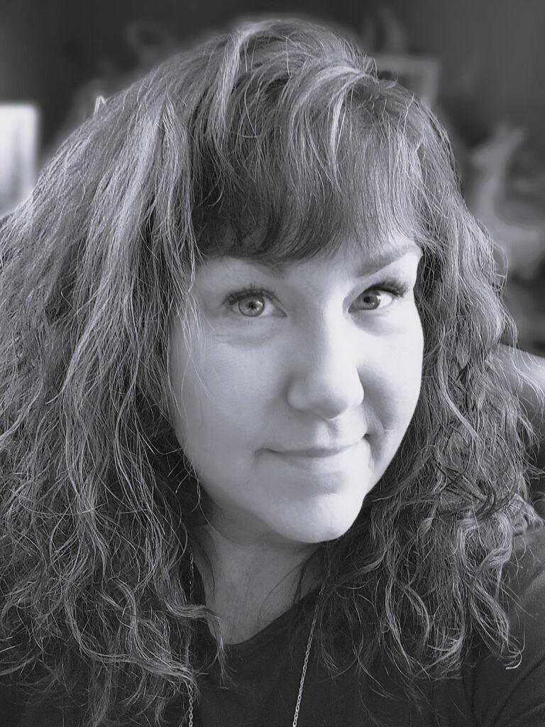 Black-and-white portrait of a woman with curly hair looking at the camera with a soft smile.