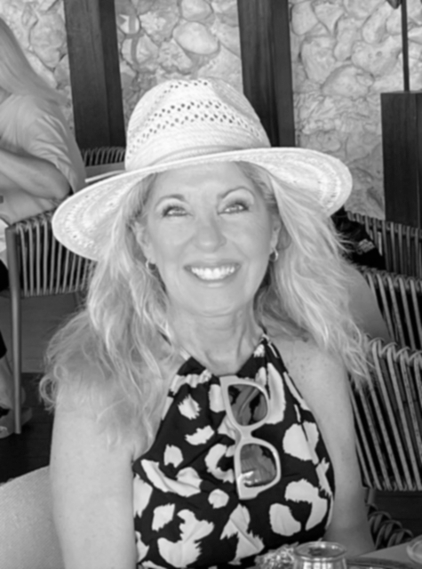 Smiling woman wearing a wide-brim straw hat and a leopard-print sleeveless top.