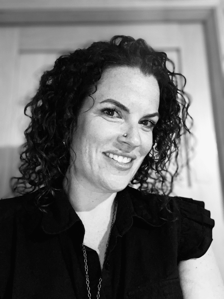 A smiling woman with curly hair wearing a dark top, looking at the camera.