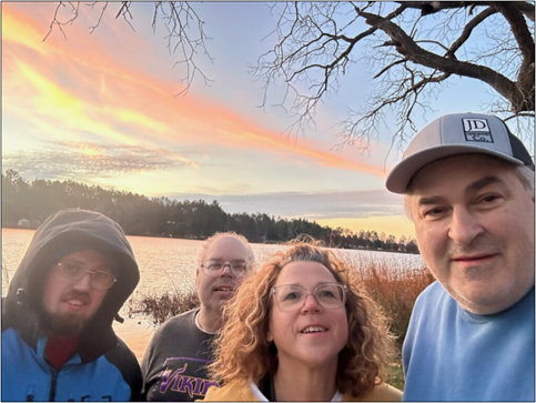 Four people in front of lake and sunset.