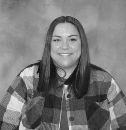Smiling person with long dark hair wearing a plaid shirt in a black-and-white portrait.