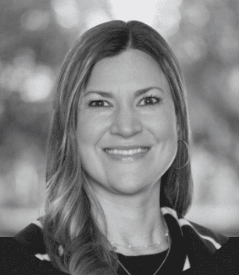 Grayscale head-and-shoulders portrait of a smiling woman with long hair outdoors.