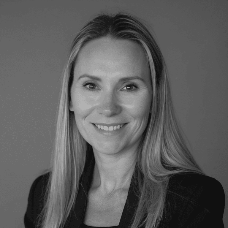 Black-and-white portrait of a smiling woman with long straight hair wearing a dark blazer.