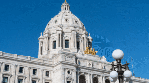 White domed neoclassical government building with a golden statue atop the dome, set against a blue sky.