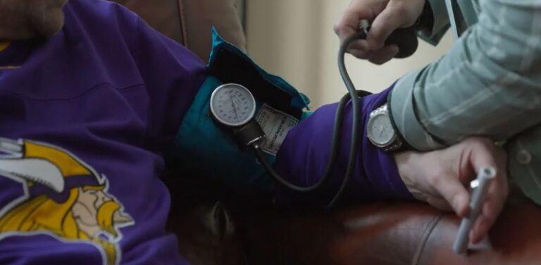 A healthcare professional checks a patient's blood pressure with a blue cuff wrapped around the upper arm.