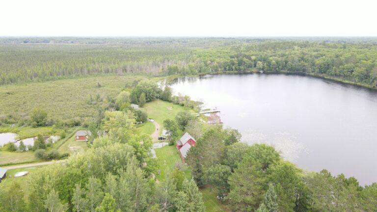 Aerial view of a lake surrounded by dense trees with a few houses along the shoreline.