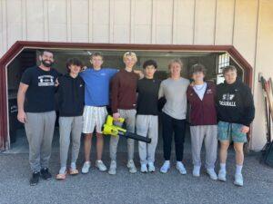 Eight people stand side by side in front of a large garage door, with one person holding a yellow toy helicopter.