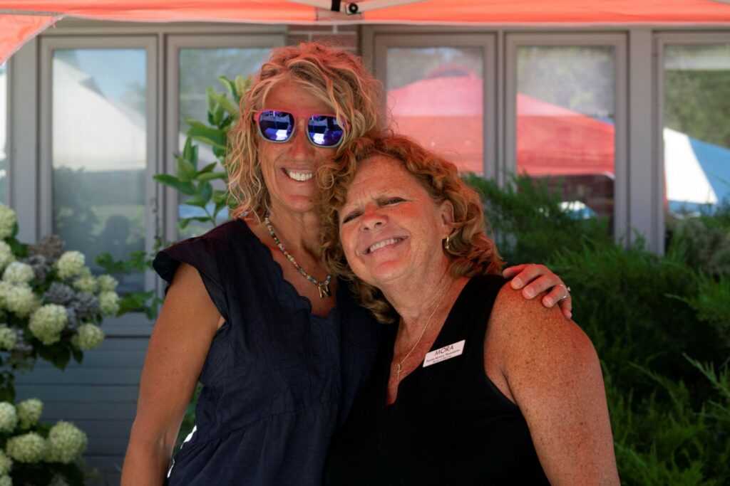 Two women stand close together outdoors, smiling with their arms around each other.