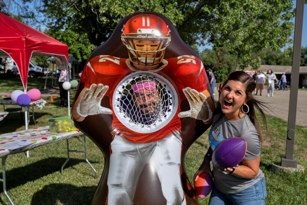 A red football mascot posing beside a smiling girl at an outdoor park.