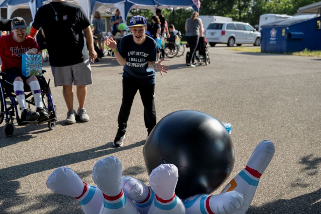 Outdoor event scene with a large black bowling ball approaching oversized striped bowling pins in the foreground.