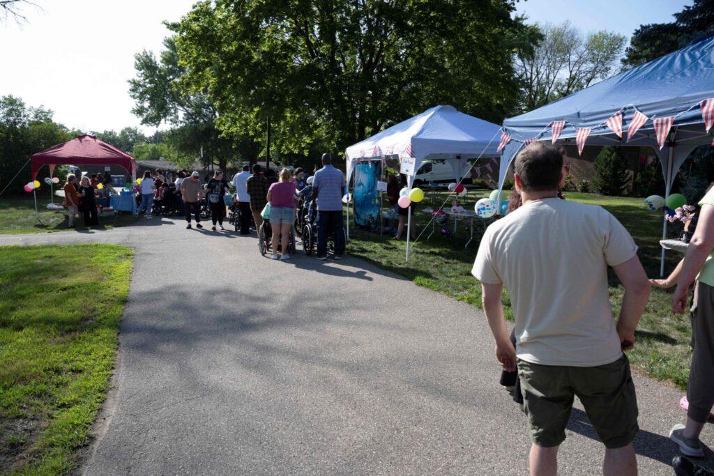 Outdoor market along a paved path with people browsing under vendor tents on a sunny day.