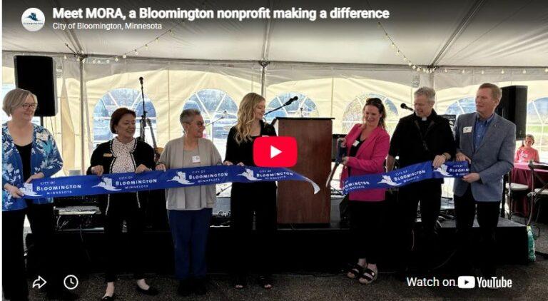 Group of people under a tent cutting a blue ribbon at a ribbon-cutting ceremony for Meet MORA, a Bloomington nonprofit.
