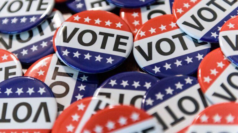 Close-up of colorful round voting buttons with the word VOTE in red, white, and blue.